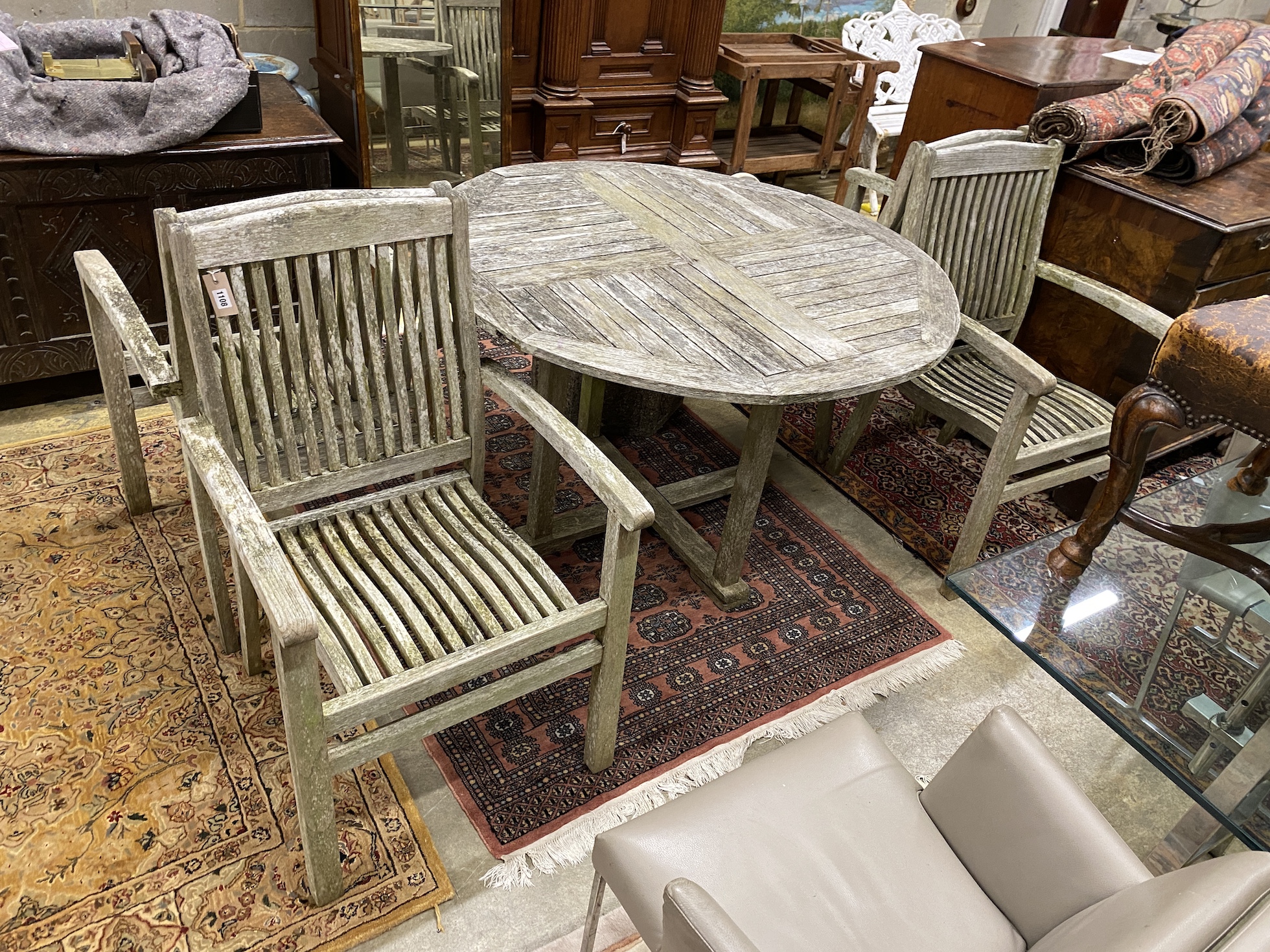 A circular weathered teak garden table, diameter 120cm, height 75cm and four elbow chairs
